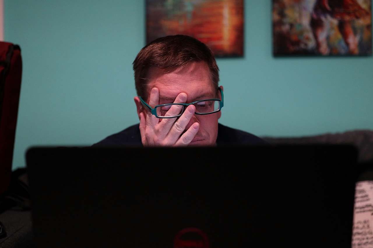Man rubbing his eyes while working at a laptop