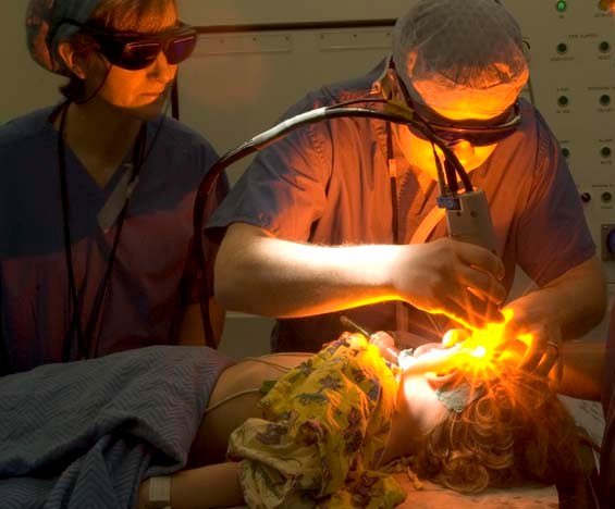 Surgeon using an ophthalmic excimer laser while an assistant observes through protective goggles