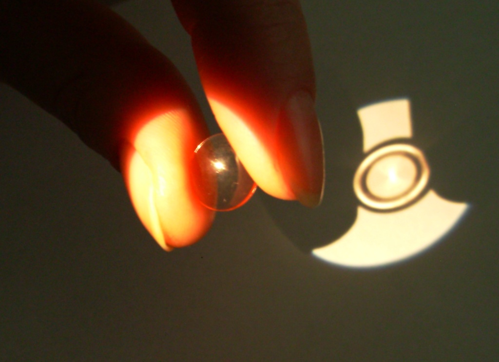 Orthokeratology lens held between fingers under bright light