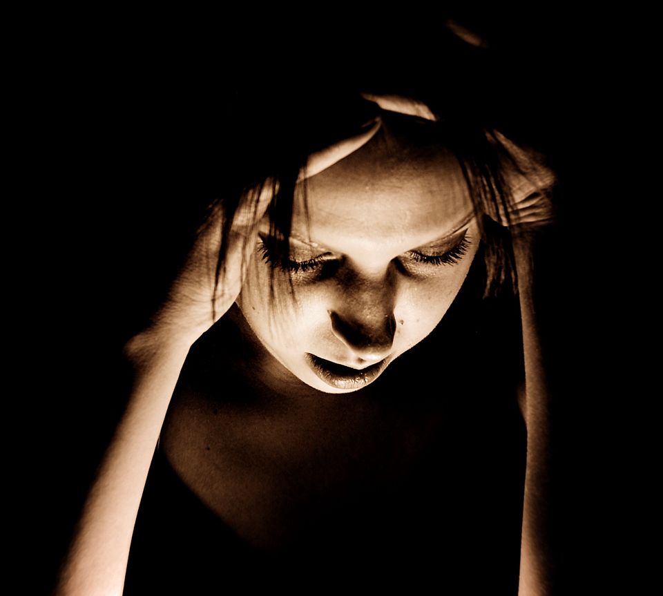 Person holding head in dark room during migraine