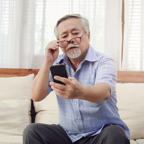 Older man holding a smartphone at arm’s length while lifting his reading glasses
